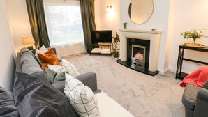 A living room with a sofa, a fireplace, a television, and a window with curtains. - Maple House (Tadcaster)