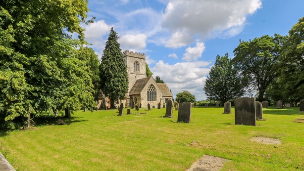 A cemetery with a prominent church in the background, surrounded by lush greenery and tombstones. - Maple House (Tadcaster)