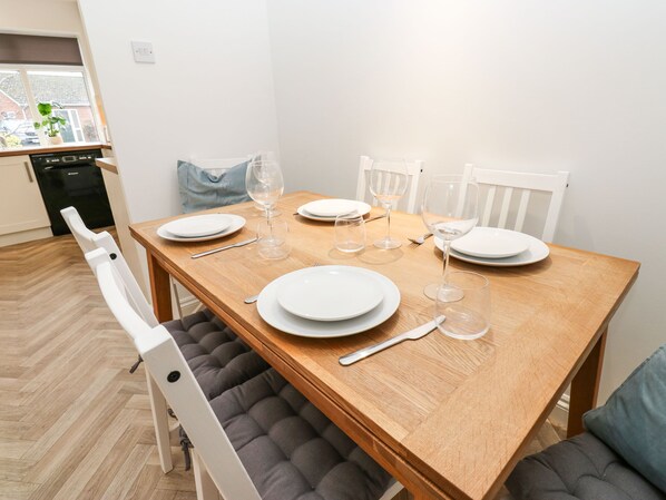 A dining table set with white plates, wine glasses, and cutlery, surrounded by cushioned chairs.