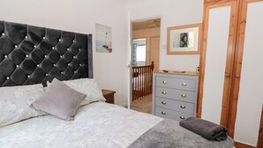 A bedroom with a tufted headboard, a floral bedspread, a grey blanket, a wooden dresser, and a mirror on the wall.