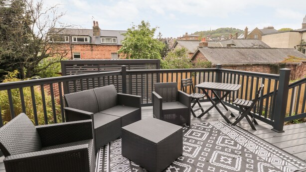 A deck with wicker furniture, a patterned rug, and a view of surrounding buildings.
