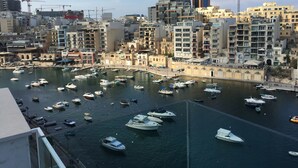 A marina with numerous boats docked, surrounded by a cityscape with various buildings and construction cranes.