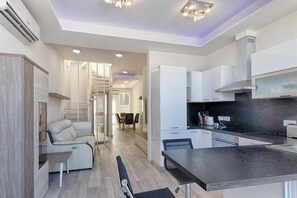 A modern kitchen with white cabinetry, a black countertop, and a dining area with a sofa and table. - Seafront Penthouse Triplex- Roof Terrace & Hot Tub (St. Julian's)