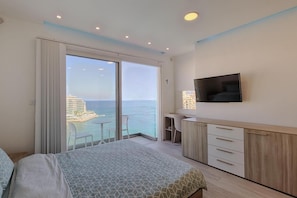 Una habitación de hotel con una cama, escritorio, televisor y vista al océano.
