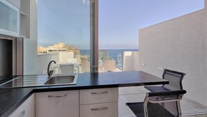 A modern kitchen with a large window, a sink, and a dining area with a chair.