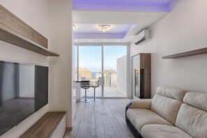 A modern living room with a large flat-screen TV, a sofa, and a dining area with a table and chairs. - Seafront Penthouse Triplex- Roof Terrace & Hot Tub (St. Julian's)