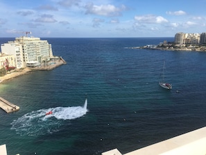 A coastal view with a marina, a sailboat, and a large hotel building. - Seafront Penthouse Triplex- Roof Terrace & Hot Tub (St. Julian's)