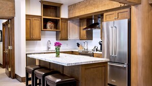 A kitchen with wooden cabinets, a stainless steel refrigerator, a marble countertop, and two bar stools. - Luxury Three Bedroom Suite with Mountain Views and Three Hot Tubs 3 Apartment Hotel by RedAwning (Park City)