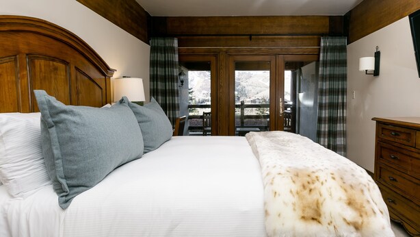 A bedroom with a large bed, wooden headboard, and a view of mountains through the door. - Deluxe King Room With Deck Hotel Room by RedAwning (Park City)