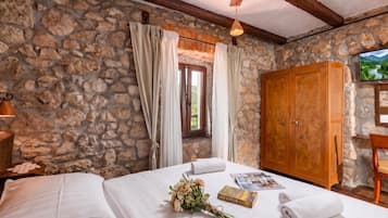 Un dormitorio con paredes de piedra, un armario de madera, una cama con ropa blanca, una ventana con cortinas y un televisor en la pared.