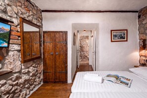 Une pièce avec un mur en pierre, une armoire en bois, un lit avec une literie blanche et un tableau encadré au mur.
