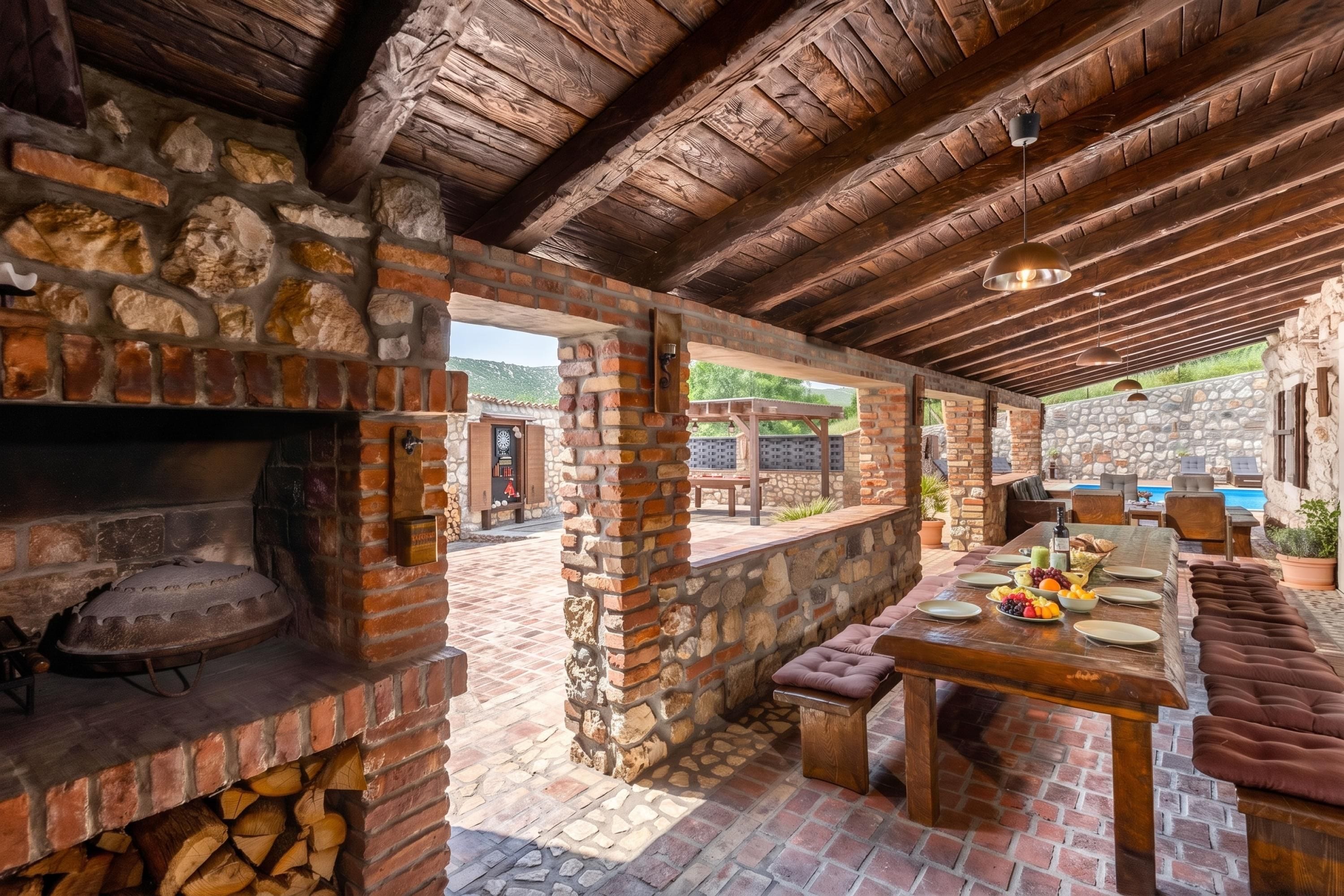 A rustic outdoor kitchen with a brick oven, stone walls, and a dining area with a table set for a meal.