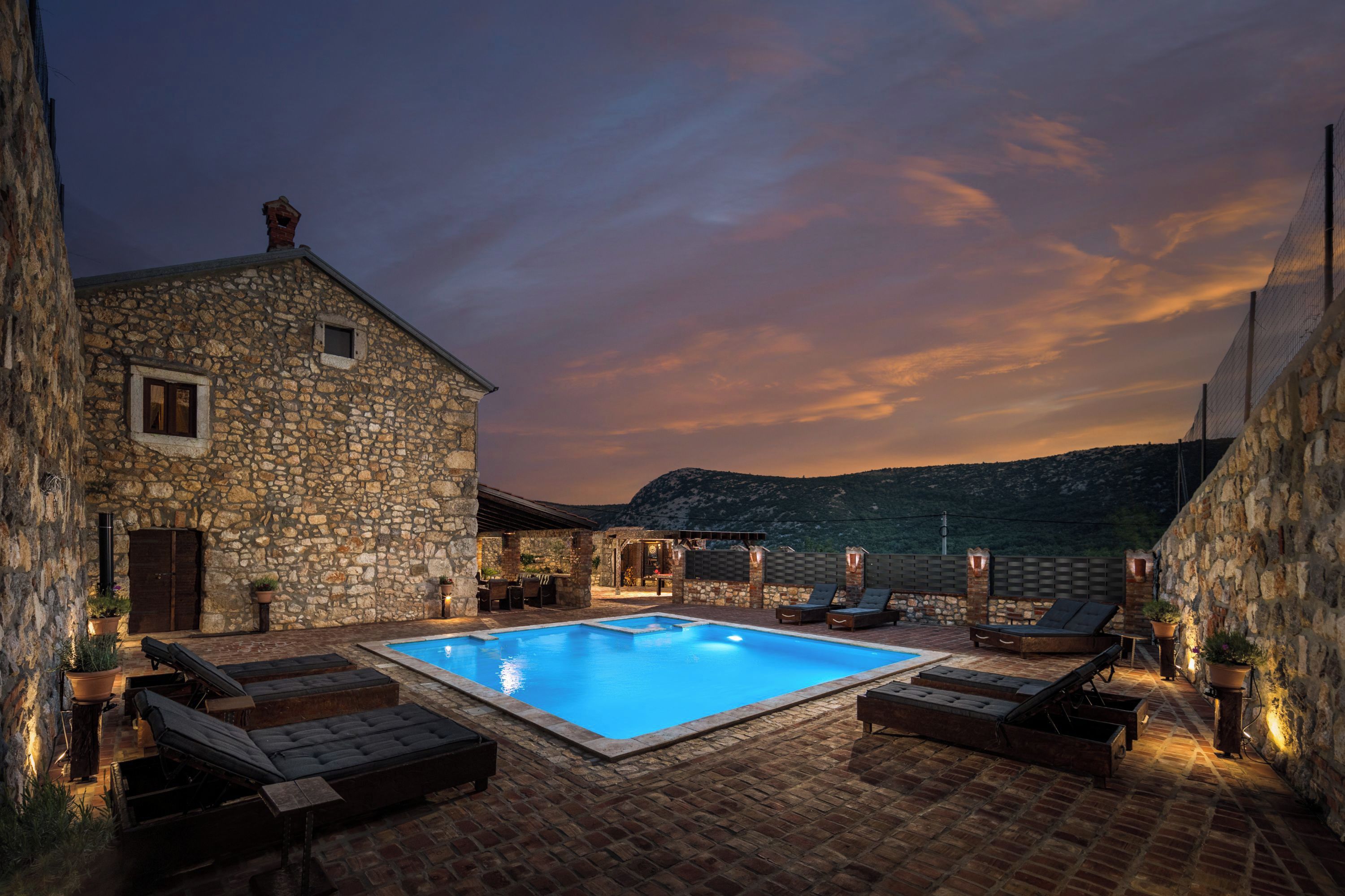 Un edificio in pietra con piscina, sdraio e area relax all'aperto.