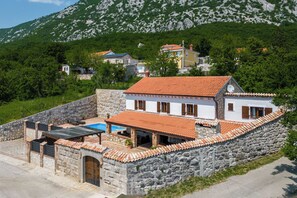 Une maison aux murs de pierre, surmontée d’un toit en tuiles, dotée d’une piscine et d’un escalier en pierre menant à l’entrée.