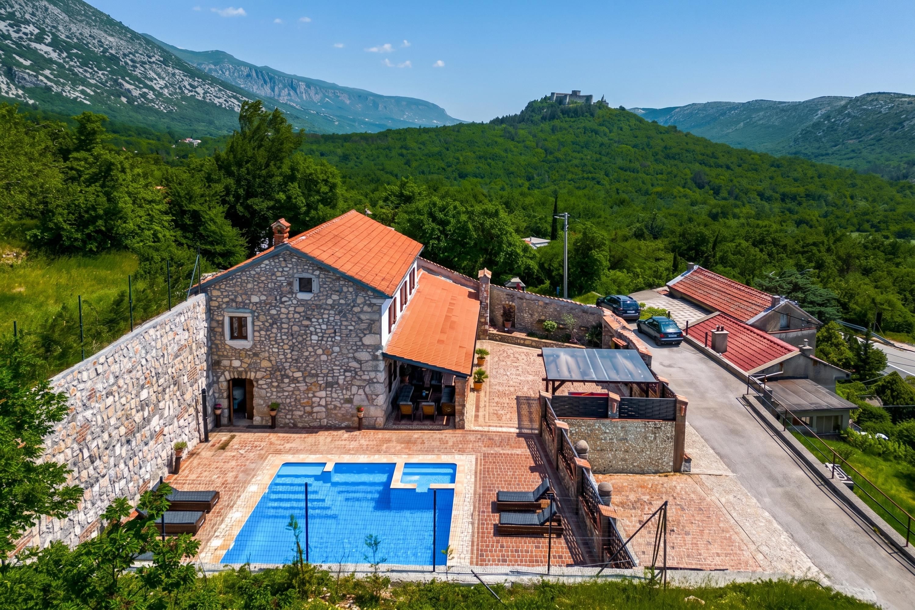 A stone building with a swimming pool, surrounded by greenery and mountains.
