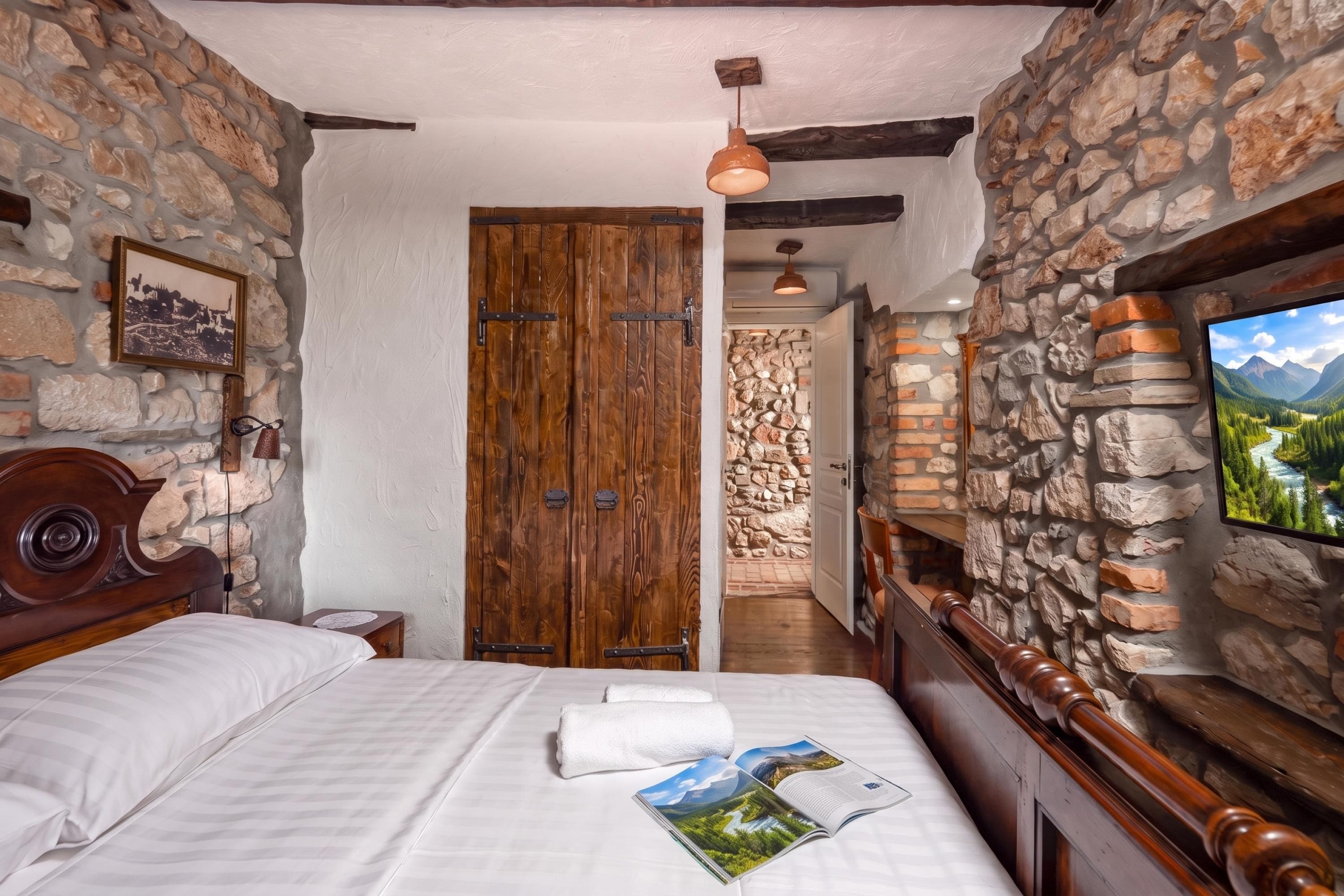 Een slaapkamer met een houten bed, een stenen muur, een houten kledingkast en een aan de muur bevestigde televisie.