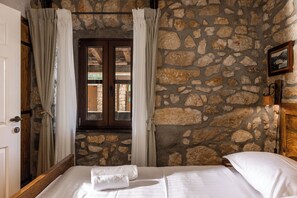 A room with stone walls, a wooden bed, and a view through a window with curtains. - Villa Cupido With Private Pool (Vinodol)