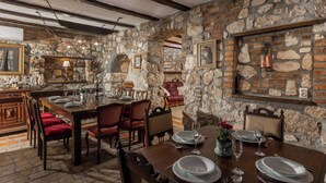 A stone-walled dining area with a wooden table set for four, red upholstered chairs, and a stone fireplace. - Villa Cupido With Private Pool (Vinodol)