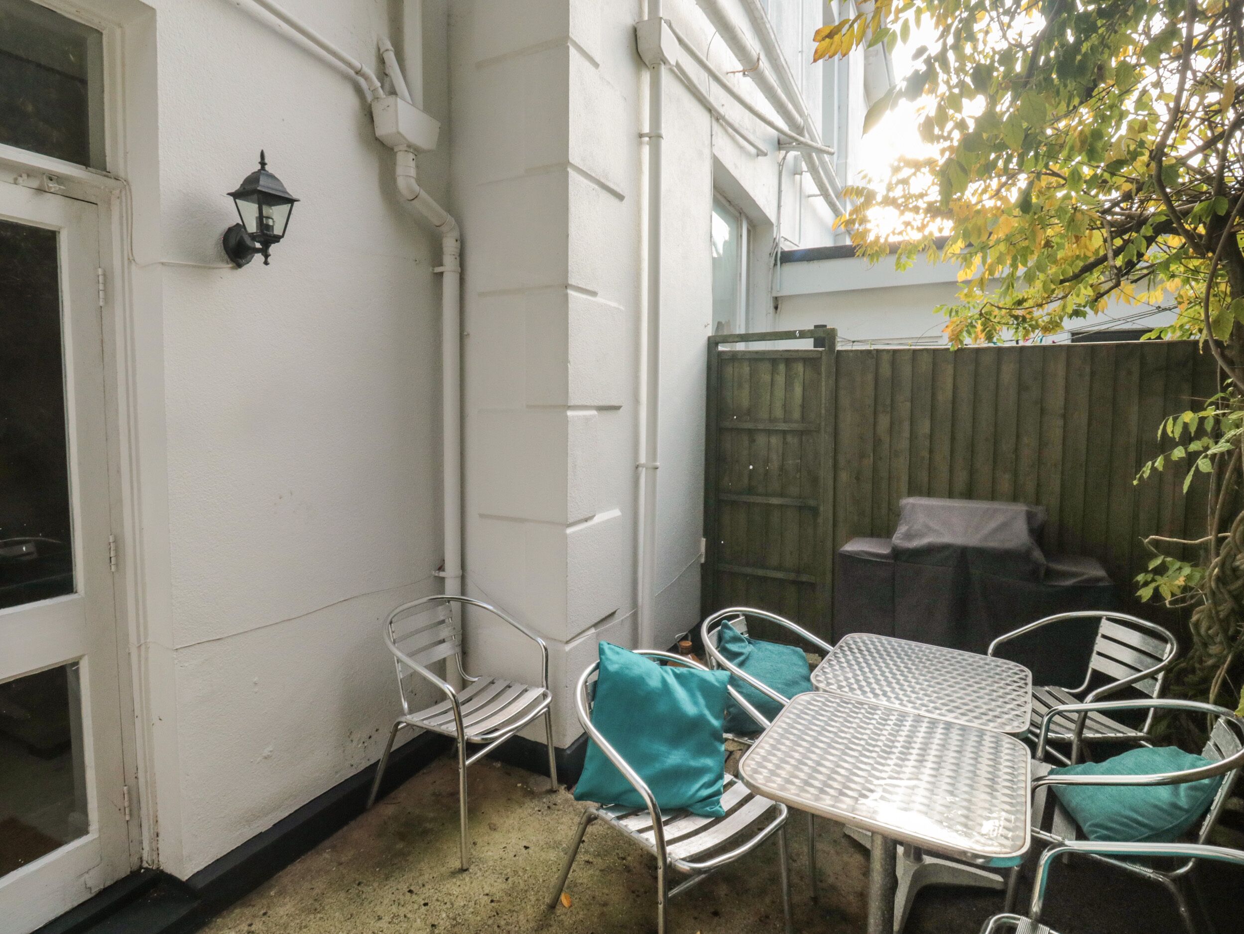 A patio with metal chairs and a table, a wooden fence, and a wall-mounted light fixture.