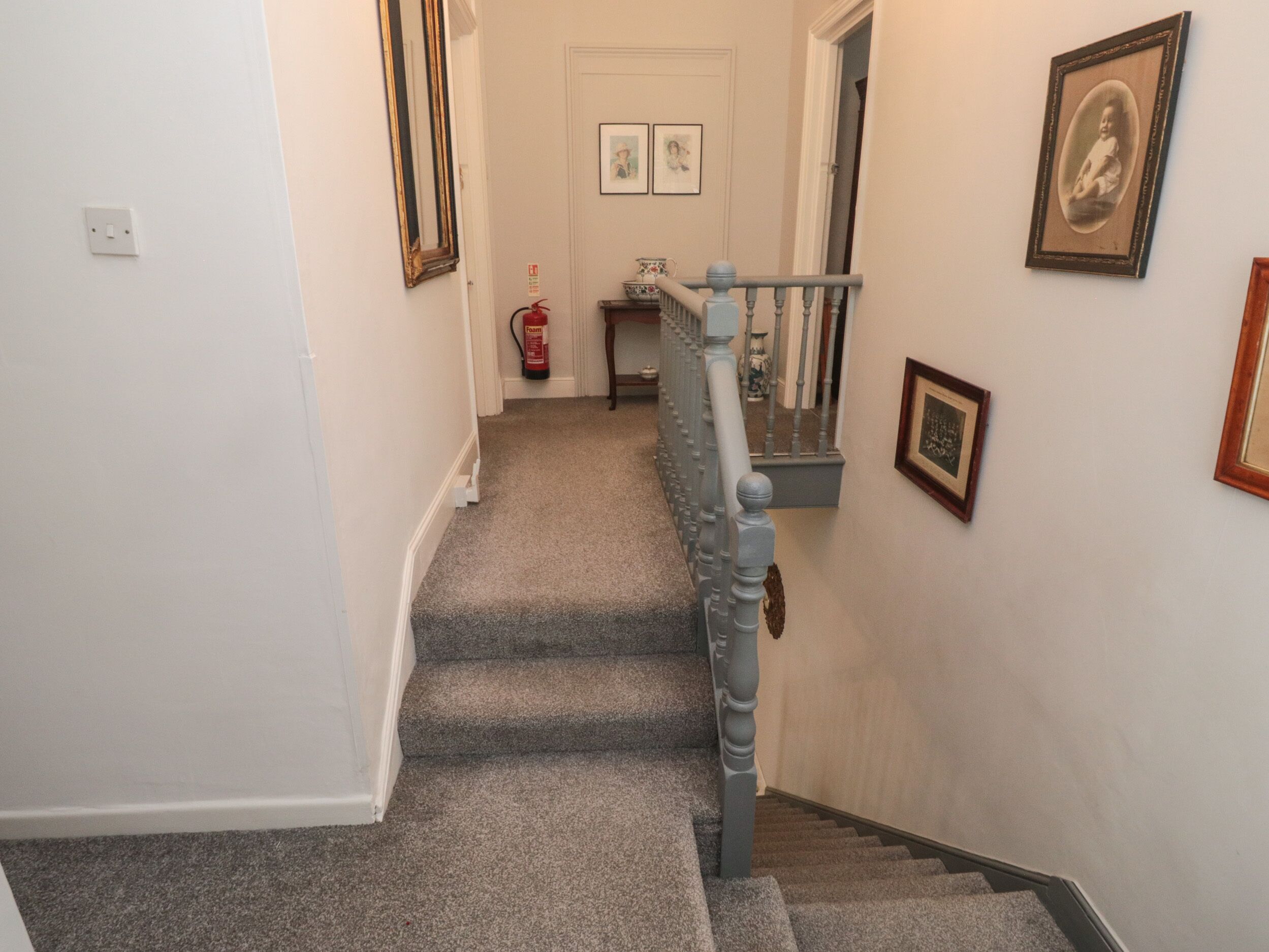 A carpeted staircase with a handrail, a fire extinguisher, and framed pictures on the walls.
