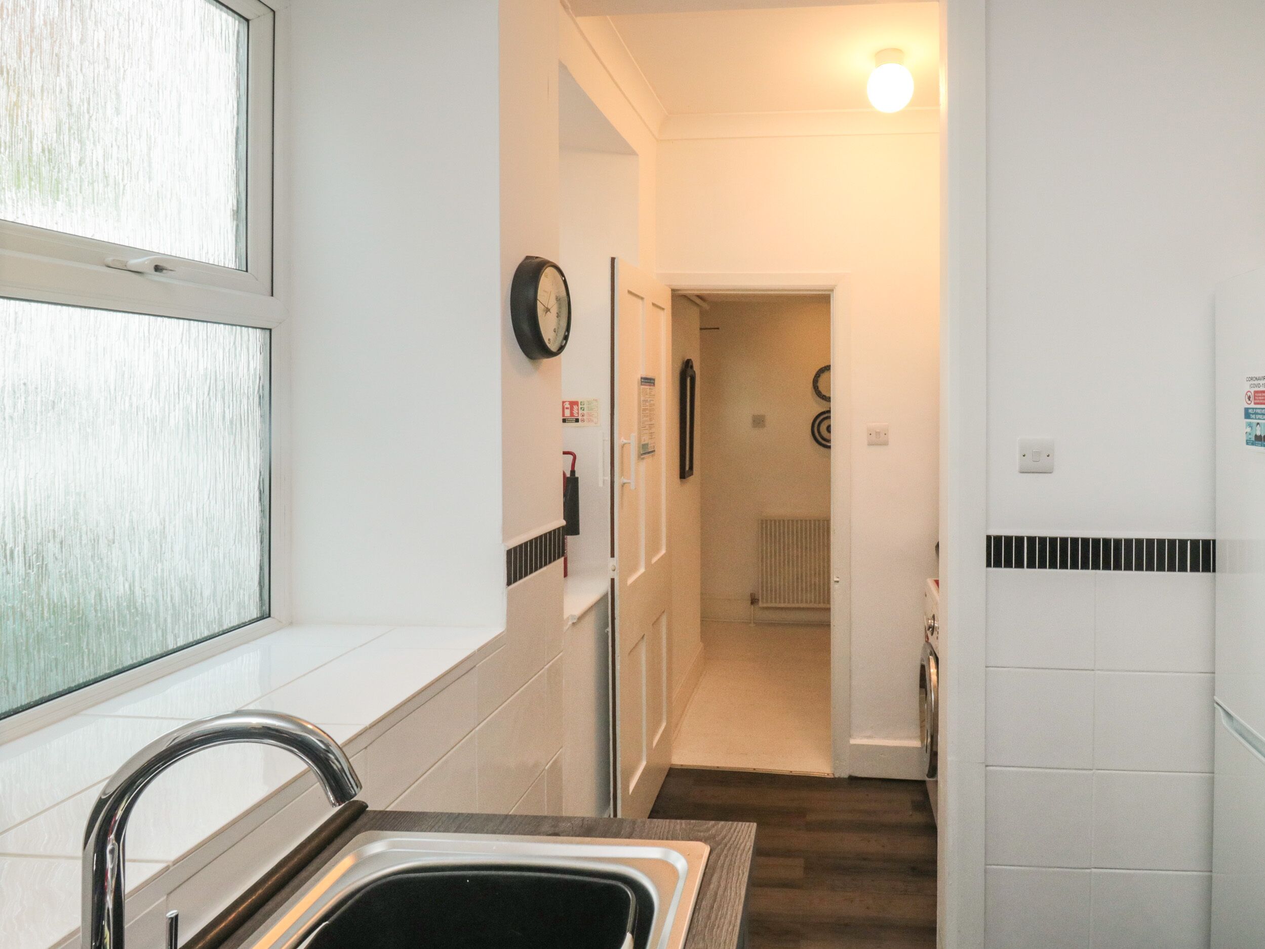 A narrow kitchen with a sink, a clock, and a radiator.