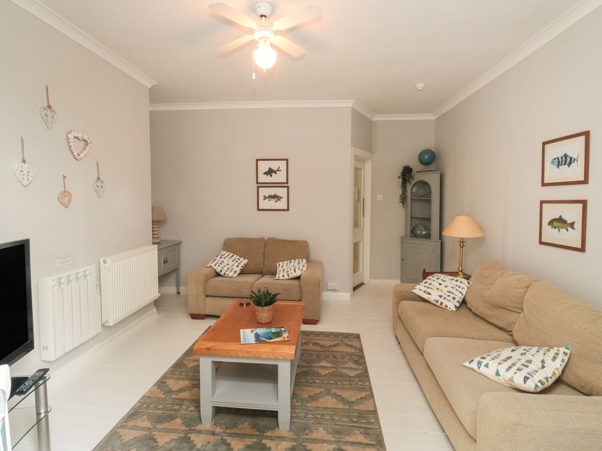 A living room with a beige sofa, a coffee table, a TV, and a ceiling fan.