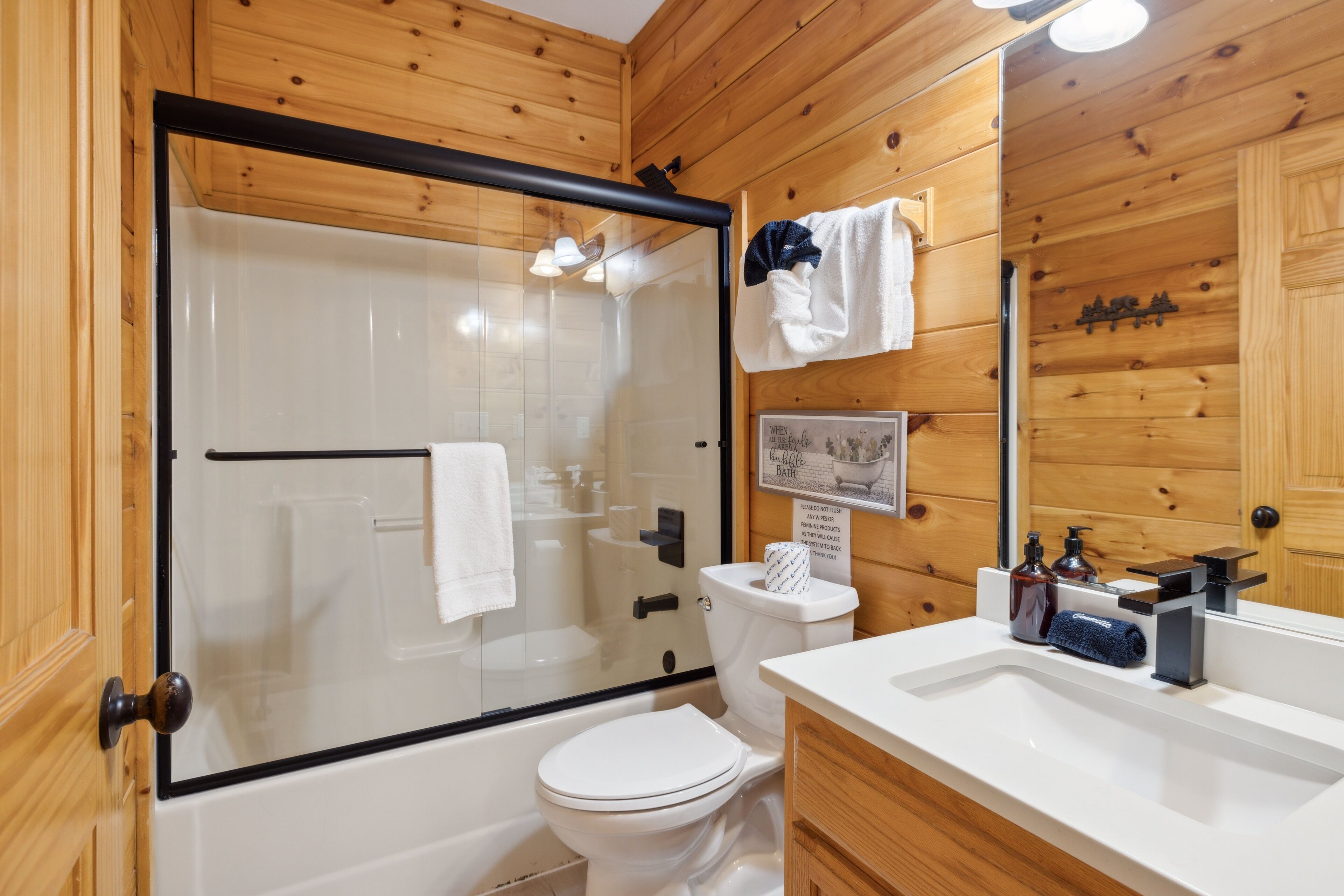 A wooden-paneled bathroom with a glass-enclosed shower, a white toilet, and a sink with a mirror.