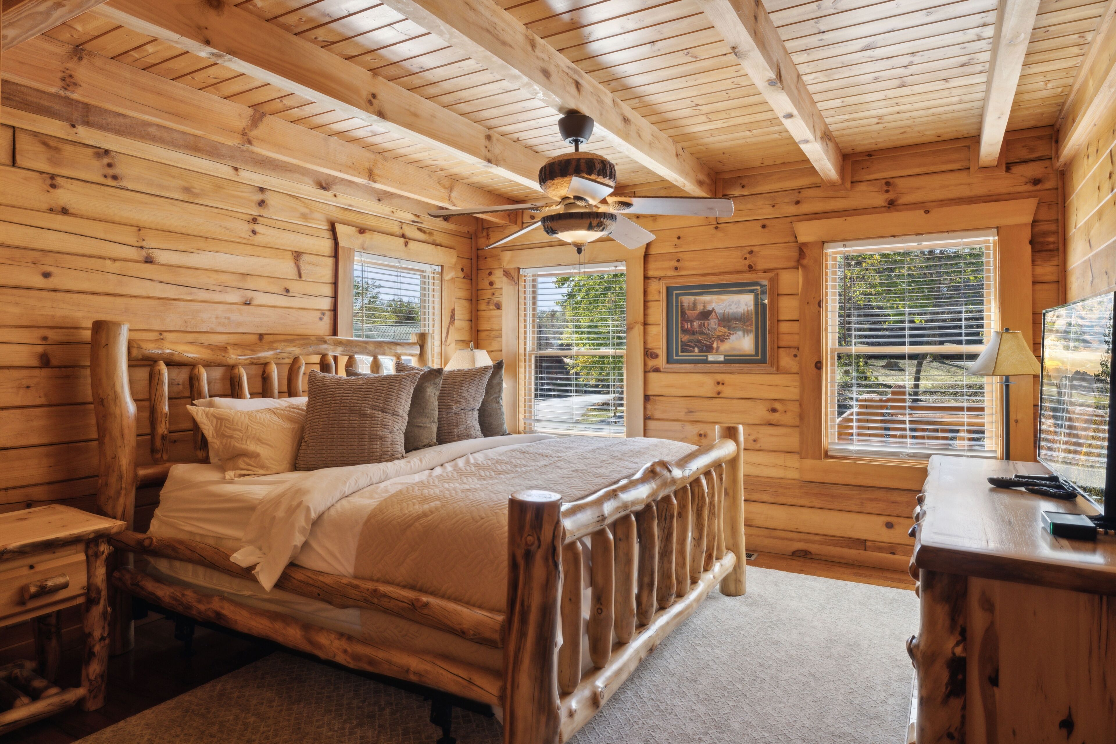 A wooden cabin bedroom with a bed, a desk, and a ceiling fan.