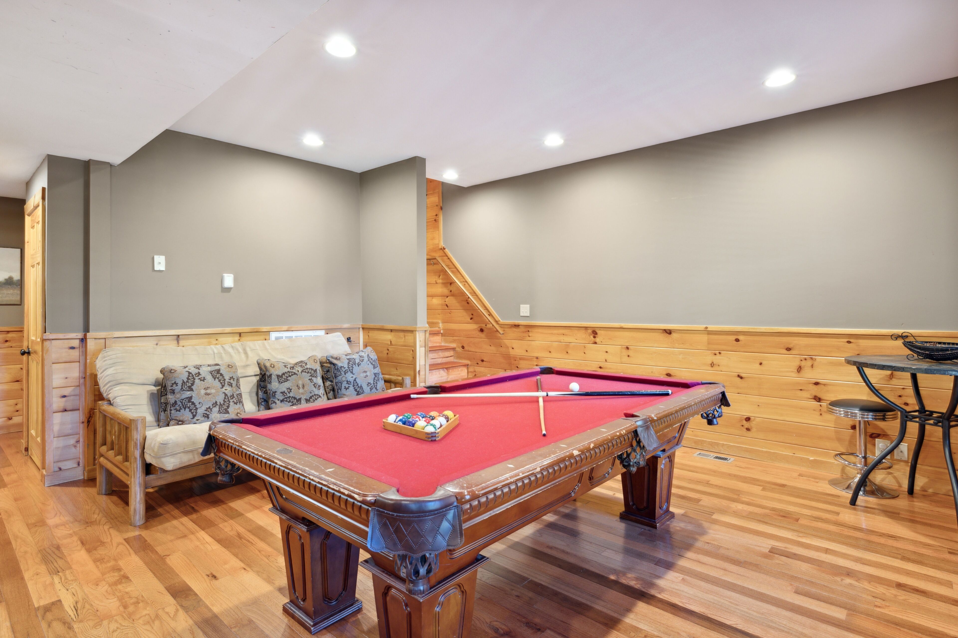 A pool table in a room with wooden walls and a sofa.