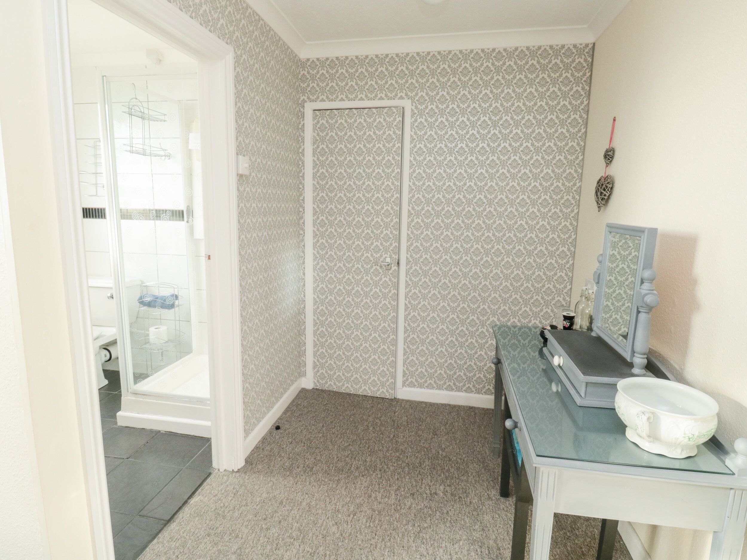 A bathroom with patterned wallpaper, a glass shower enclosure, a vanity with a mirror, and a bowl on the counter.