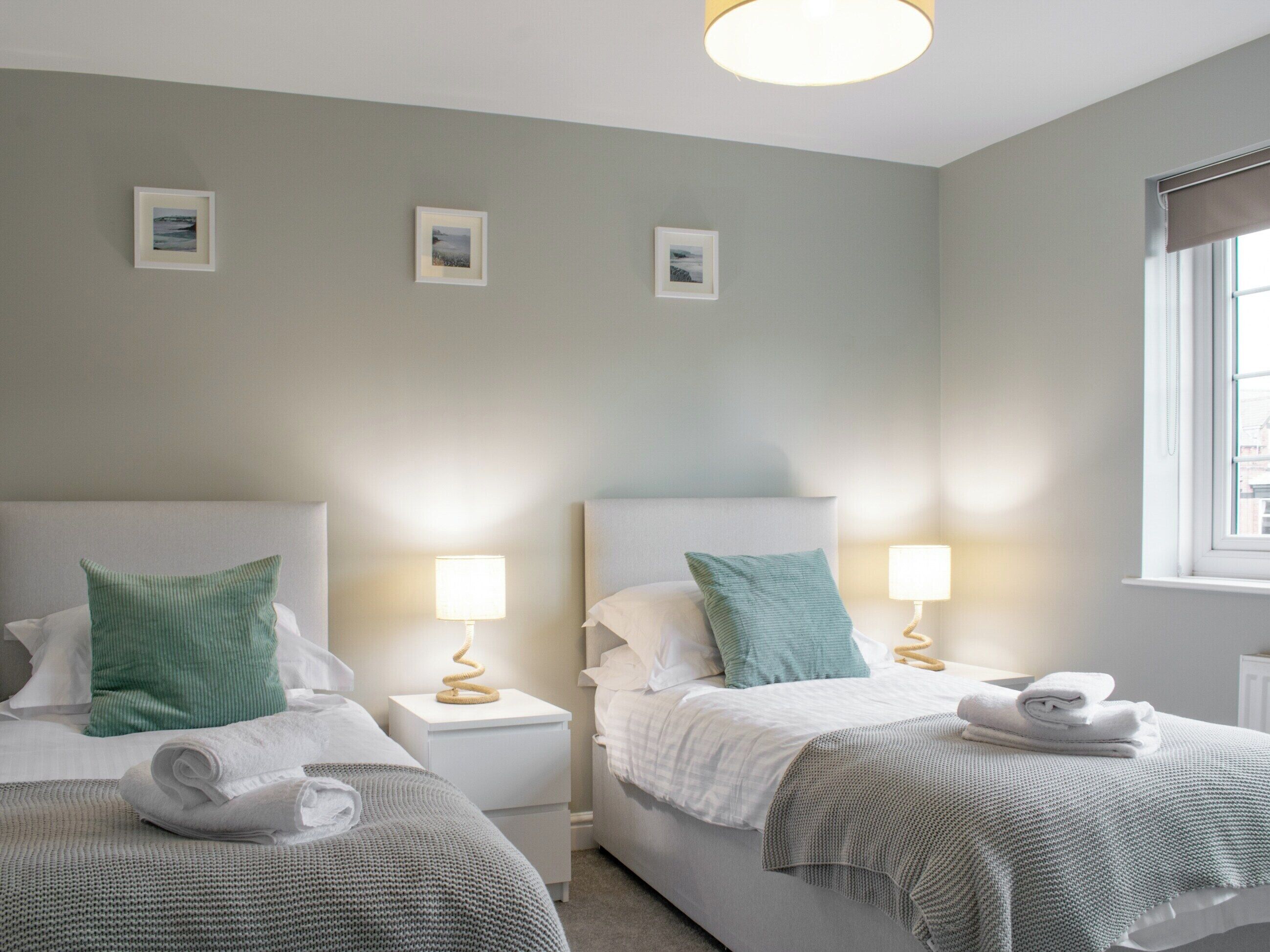 Una habitació d'hotel amb dos llits, cada un amb un coixí i una làmpada. Hi ha tres quadres al mur.