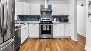 A modern kitchen with white cabinets, stainless steel appliances, and a blue tiled backsplash. - Jeff GNV Home #1 · Renovated 3/2+ bonus, Heart of Gville, UF+Springs (Gainesville)