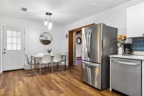 A modern kitchen with stainless steel appliances, a dining area with white chairs, and a wooden floor.