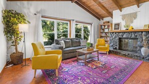 A cozy living room with a sofa, two armchairs, a coffee table, a large rug, a fireplace, and a bookshelf. - Jeff GNV Home #1 · Renovated 3/2+ bonus, Heart of Gville, UF+Springs (Gainesville)