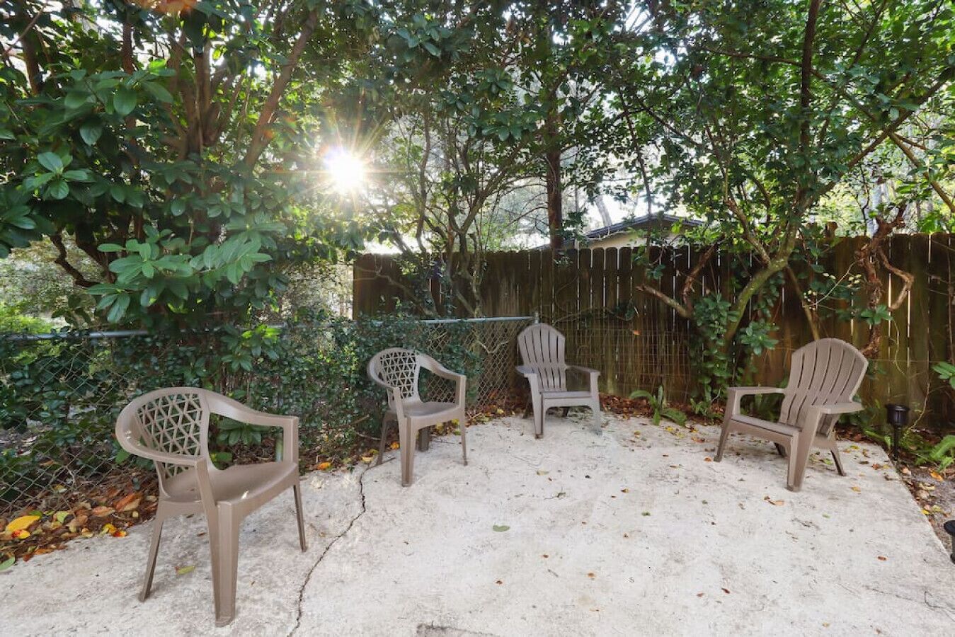 An outdoor seating area with three chairs and a concrete floor, surrounded by a fence and trees.