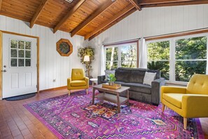 A cozy living room with a wooden ceiling, a patterned rug, a sofa, two armchairs, and a coffee table.