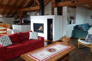 A cozy living room with a fireplace, red sofa, wooden coffee table, and a teal armchair.