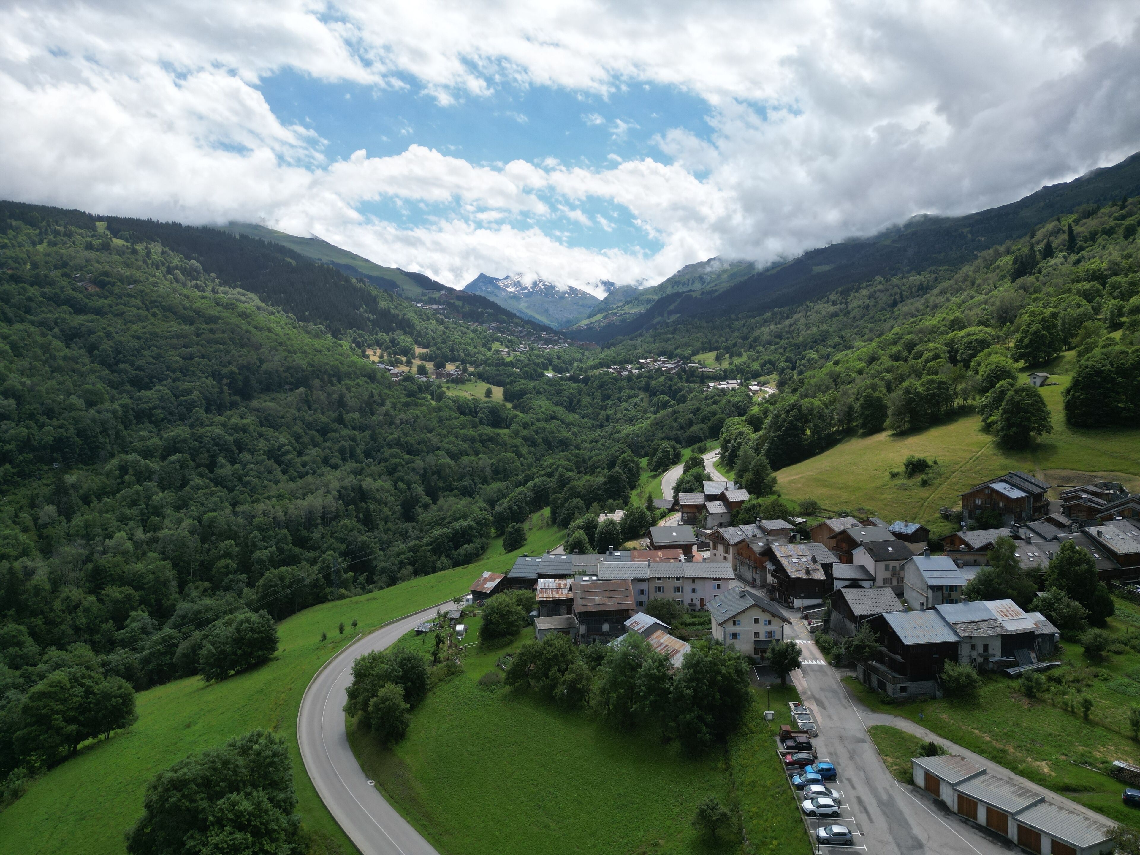 Un pueblo enclavado en un valle con un camino serpenteante, rodeado de colinas y montañas verdes y exuberantes.