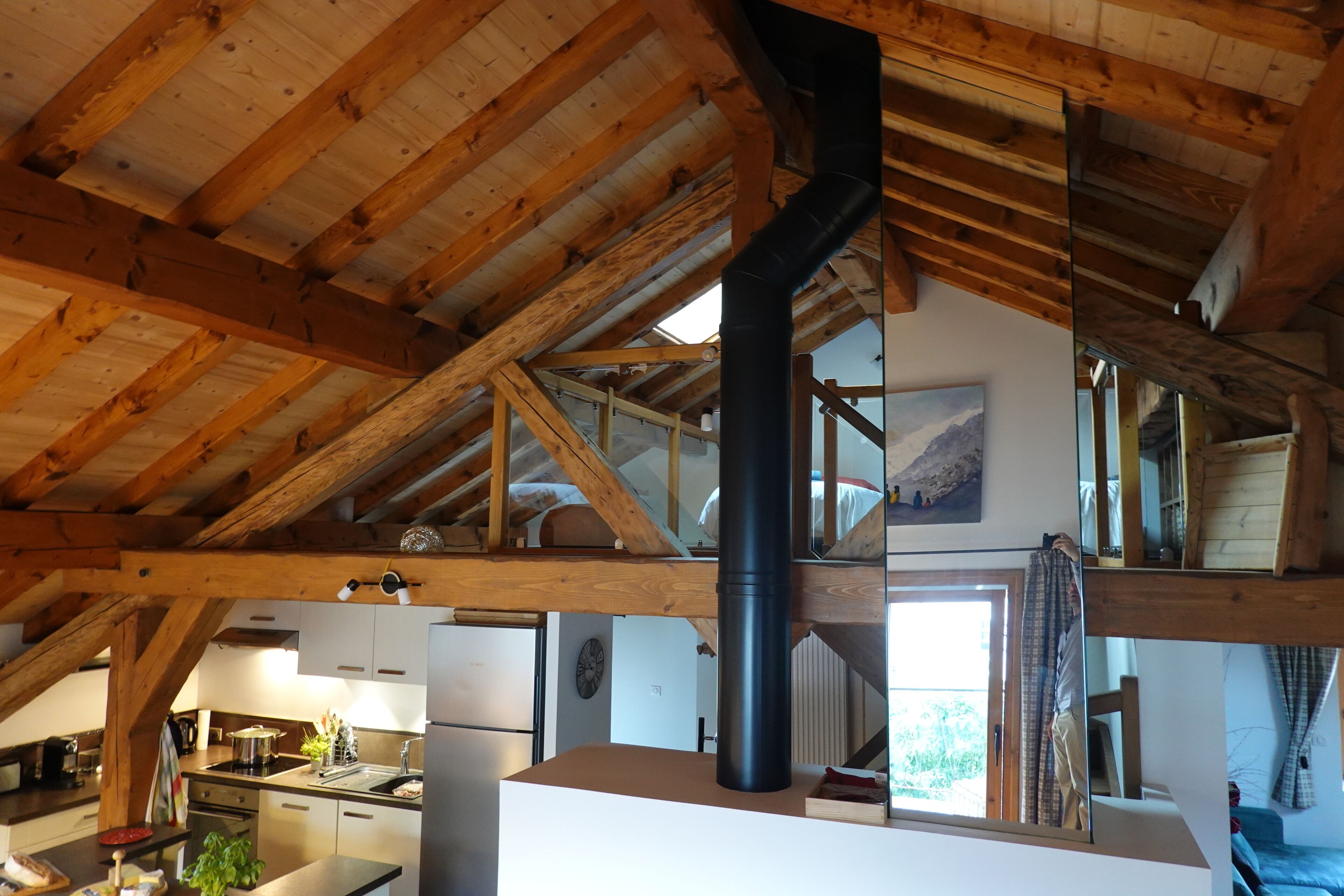Una cocina rústica con vigas de madera, una chimenea negra y vistas al exterior.