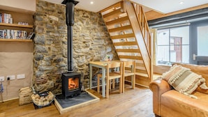 A cozy living room with a stone wall, a fireplace, a wooden staircase, and a leather sofa.