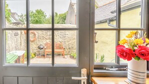A room with a large window divided into four panes, a wooden bench, a small table, and a vase with flowers.