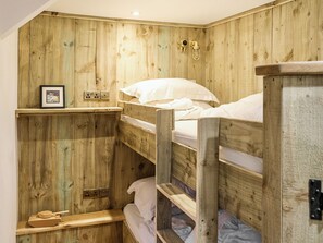 A bunk bed room with wooden walls, a shelf with a picture, and a small wooden table.