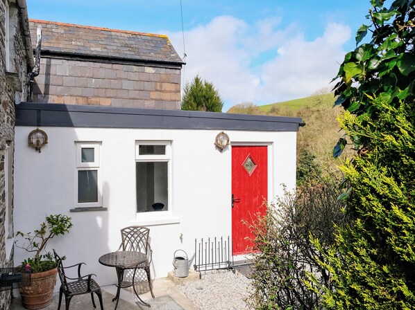 A small white building with a red door, a window, and a doorbell.