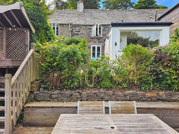 A stone house with a wooden deck, a small garden, and a modern glass extension.