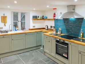 A kitchen with grey cabinets, a wooden countertop, a stainless steel range hood, and a tiled backsplash.