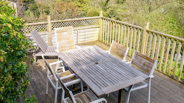 Eine Holzterrasse mit Tisch und Stühlen, umgeben von einem Holzzaun und Grünpflanzen.
