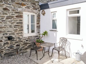 A stone wall, a white door, two metal chairs, a small round table, and a potted plant.
