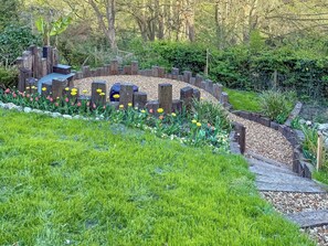 A garden with a circular wooden structure, surrounded by a variety of flowers and greenery.