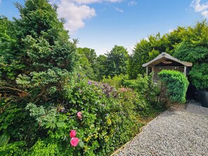 A garden with a gravel path, a wooden gazebo, and various green plants.