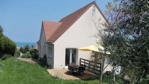 A house with a red roof, a patio with a table and chairs, and a yellow umbrella.